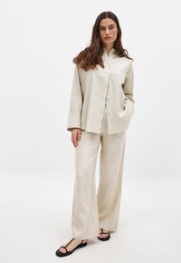 Set composto da camicia in lino beige e pantaloni a gamba larga, con chiusura frontale a bottoni, vestibilità comoda e grandi polsini. Abbinato a sandali neri flat.