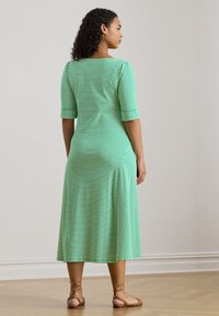 Green and white striped midi dress with a fitted bodice, three-quarter sleeves, and a flared skirt. Worn with brown strappy sandals.