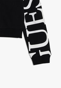 Czarna bluzka z długim rękawem z dużymi, białymi, wyraźnymi literami drukowanymi w pionie, z ściągaczem na nadgarstku.