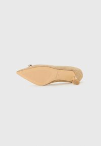 Beige suede kitten heel shoe with pointed toe, visible sole texture, and a small buckle detail near the front.