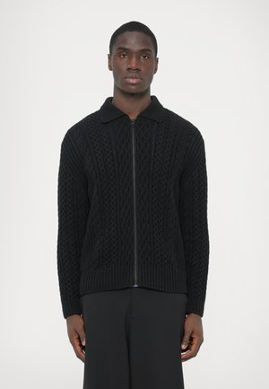 Czarny sweter rozpinany na zamek z kołnierzem, o teksturze z dzianiny warkoczowej i prążkowanym obszyciu. Długie rękawy i lekko dopasowany krój.