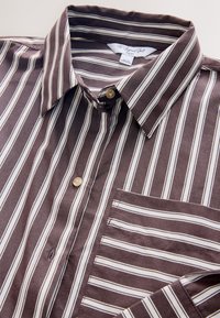 Camicia a righe marroni e bianche con bottoni, in cotone, con colletto, taschino sul petto e bottoni color terra, con una texture liscia.