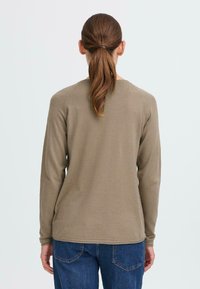 Langermet olivengrønn genser med rund hals, ribbede mansjetter og glatt tekstur, kombinert med blå denimjeans.