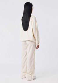Cr�ème-kleurige, oversized sweatshirt met elastische manchetten, gecombineerd met bijpassende losse broek. Zachte textuur, minimalistisch ontwerp en subtiele blauwe accentlijn.