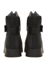 Botines negros con acabado mate, que presentan paneles laterales elásticos y una suela texturizada. Costuras reforzadas visibles a lo largo de las costuras.