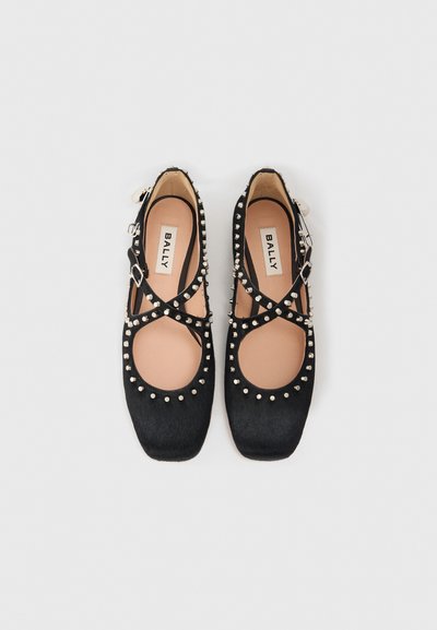 Ballerines en cuir noir avec un bout carré plat, des accents cloutés le long des bords et une sangle à la cheville en croix.