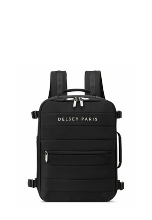 Mochila negra con textura acolchada, correas ajustables, asa superior y acentos de hardware plateado. Logo "DELCY PARIS" mostrado en la parte frontal.