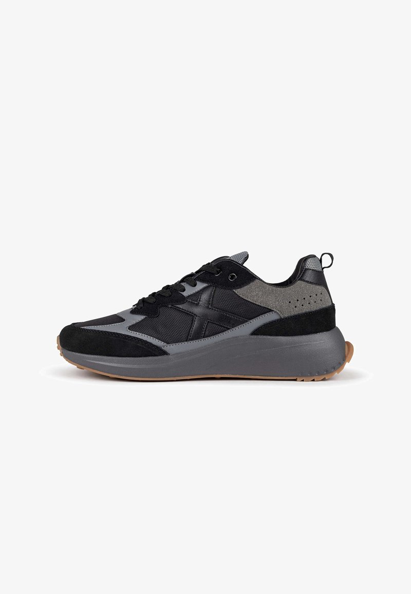 Zapatillas deportivas en negro y gris que presentan materiales de ante y malla, una puntera redondeada, una entresuela acolchada y una suela exterior de goma texturizada.