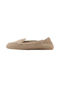 Mocasines de ante beige con suela plana, que cuentan con una textura suave, costuras sutiles y un diseño sin cordones sin hardware visible.