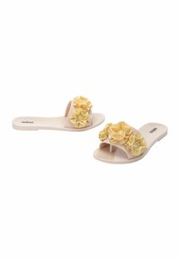 Chanclas de color rosa claro con un gran adorno floral amarillo en la correa. Material suave con suela plana y diseño de punta abierta.