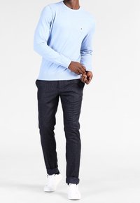 Ljusblå stickad tröja, marinblå texturerade byxor och vita sneakers. Tröjan har rundad halsringning och tighta ärmslut. Byxorna har uppvikta fållar.