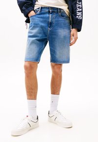Denimbukser i lys blå, klassisk snitt med fem lommer og beltehemper. Kombinert med hvite sneakers og stripete hvite sokker.