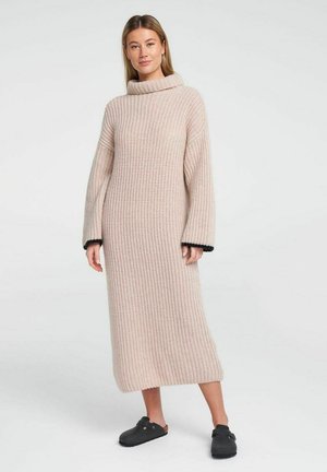 Light pink knitted dress with a cowl neck, long sleeves, ribbed texture, and black trim at the cuffs, reaching mid-calf.