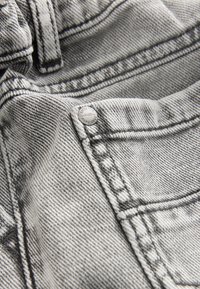 Close-up of gray denim jeans showing stitching, belt loop, front pocket, and metal rivet with text and numbers.