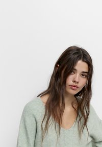 Pulover tricotat de culoare verde deschis, cu decolteu în V, textură moale și croială lejeră, având mâneci lungi și o cădere relaxată.