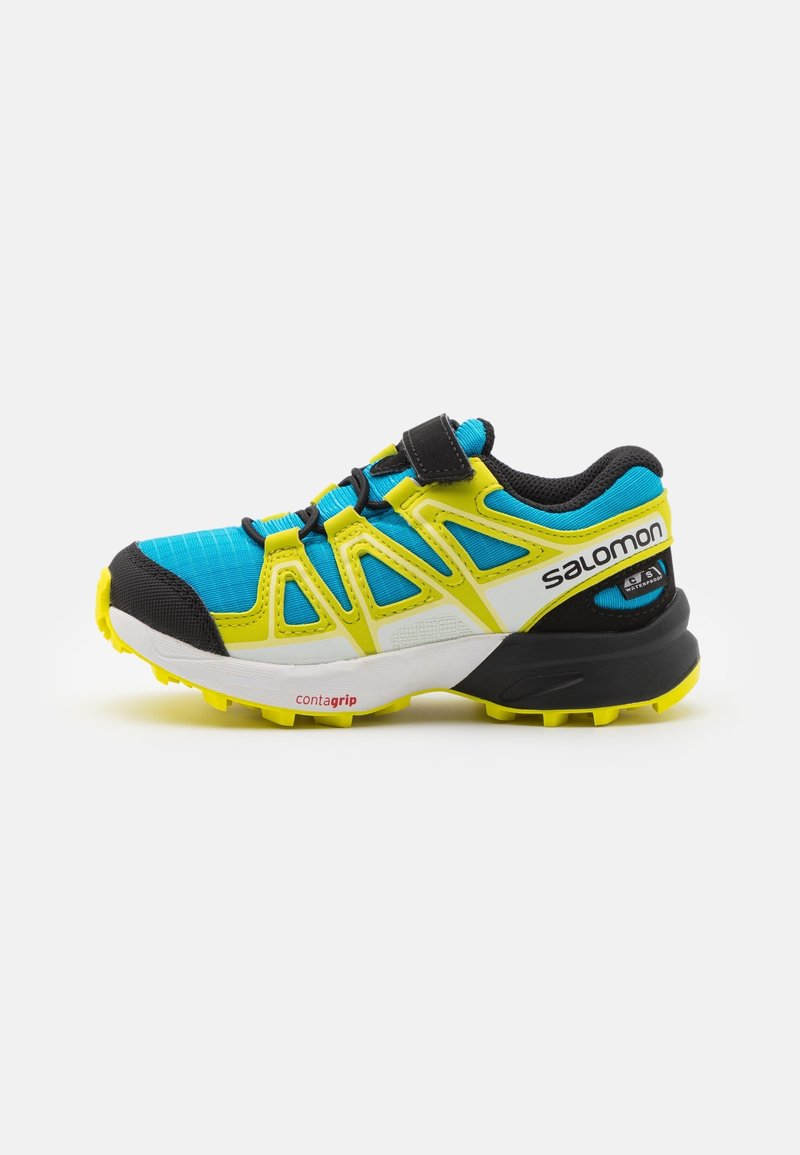 Running shoe with a blue mesh upper, yellow accents, and black details. Features a Velcro strap and a textured rubber sole.
