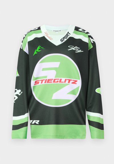 Jersey de manga longa verde e preto com logótipo circular, gráficos em branco e vermelho em destaque, e design em forma de V. Feito de tecido respirável.