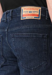 Tumedad sinine teksarihm, millel on nahklabel, millel on tekst "Diesel Industry". Viie-taskuga disain, tagaküljel on pintselduse detailid.
