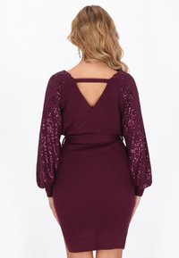 Burgundowa dopasowana sukienka z długimi rękawami akcentowanymi cekinami oraz tyłem w kształcie litery V. Żebrowana tekstura z wyraźnie podkreśloną talią. Ogólnie elegancka konstrukcja.