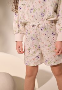 Kwiatowe szorty z kremowej tkaniny z wielokolorowymi wzorami kwiatowymi, elastyczną talią i sznurkiem do regulacji. Dopasowane mankiety u dołu.