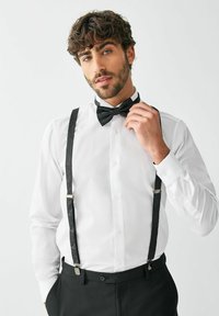 Valge kleit-särk musta mustriga õlarihmade ja kikilipsuga. Nööbitud krae, pikad varrukad ja mansetinööbid, kantud mustade pükste kohal.