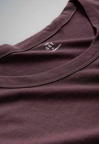 Mørkelilla t-shirt med crew neck, der viser indvendig halsmærkat med mærkenavn "THE SET" og størrelse "M".