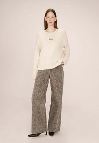 Maglione crema con la scritta "oui" ricamata in rosso. Pantaloni a gamba larga con stampa animale grigia. Il modello indossa scarpe nere con tacchi; texture morbide e vestibilità rilassata visibili.