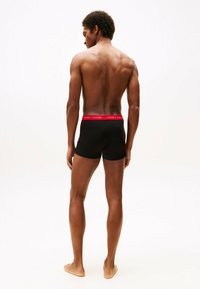 Schwarze Boxershorts mit rotem Bund, auf dem der Text "TOMMY HILFIGER" steht. Der Stoff wirkt glatt und eng anliegend.