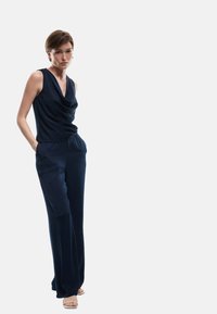 Top sin mangas de color azul marino con cuello de capa, combinado con pantalones de pierna ancha y corte holgado. Textura de tela suave, diseño minimalista.