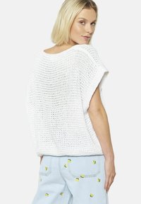 Maglione bianco a maglia oversize con maniche corte, caratterizzato da una vestibilità ampia e un motivo testurizzato, abbinato a jeans azzurri chiari decorati con ricami floreali gialli.