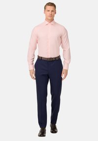 Camicia rosa chiaro con colletto alla francese, chiusa con bottoni, abbinata a pantaloni blu navy e cintura di pelle marrone, indossata con scarpe nere.