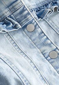 Tissu en denim bleu clair avec coutures verticales, boutons-pression métalliques argentés et détails élastiqués froncés près du bord supérieur.