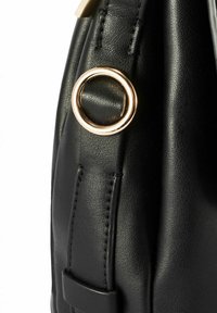 Zbliżenie czarnego skórzanego paska torby z regularnymi szwami i błyszczącym złotym metalowym pierścieniem przymocowanym do niego.