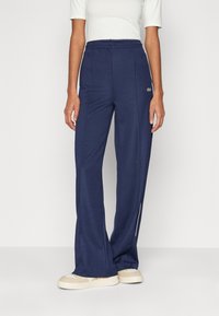 Navy wide-leg sweatpants with elastic waistband and side stripes. Fabric has a smooth texture, featuring a small logo on the left hip.