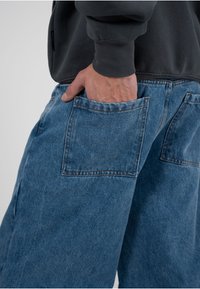 Hellblaue Denimhose mit lockerem Sitz, einer großen Gesäßtasche und sichtbaren Steppnähten. Das Material weist eine verwaschene Textur auf.