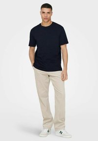 Marineblaues Baumwoll-T-Shirt mit Rundhalsausschnitt, kombiniert mit beigen Cordhosen und weißen Sneakers mit grünen Akzenten.