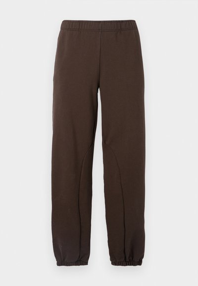 Sötétbarna melegítőnadrág elasztikus derékkal, szűkülő mandzsettákkal és diszkrét ívelt varrásokkal az oldalán. Sima pamut anyag.