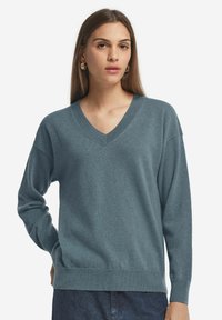 V-ringad tröja i mjukt, heathered teal tyg. Har långa ärmar, ribbade muddana och fåll, avslappnad passform och jämn textur.