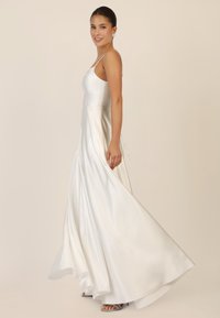 Ein ärmelloses, bodenlanges weißes Kleid mit einem taillierten Oberteil und einem A-Linien-Rock, aus glattem Satin. Es hat einen subtilen Glanz und schmale Träger.