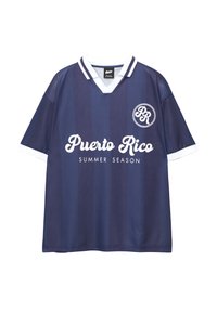 Maillot de football bleu marine avec des accents blancs, présentant des rayures verticales et le texte "SAISON D'ÉTÉ PUERTO RICO" en cursive. Logo rond sur la poitrine.