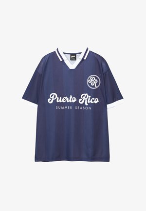Mörkblå fotbollsjacka med vita detaljer, med vertikala ränder och texten "Puerto Rico SOMMARSAISON" i kursiv stil. Rund logotyp på bröstet.