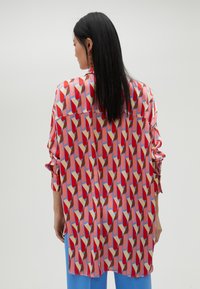 Silk shirt featuring a colorful geometric pattern in red, pink, blue, and beige. Loose fit, with long sleeves and a shirt collar.