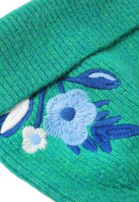 Tissu tricotat verde cu o textură ribată, având motive florale brodate în albastru și alb. Designul include diverse forme de frunze.