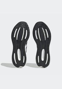 Suole di scarpe da corsa nere con grip testurizzato, caratterizzate da accenti bianchi e scanalature per una maggiore trazione, progettate per comfort e prestazioni.