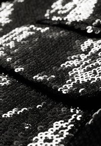 Gros plan d’un tissu noir densément couvert de sequins noirs et argentés brillants créant un motif scintillant.