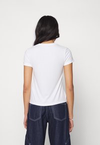 Hvid T-shirt med korte ærmer og rund hals; lavet af bomuldsmateriale med en glat tekstur; bæres med mørke, brede denimbukser.