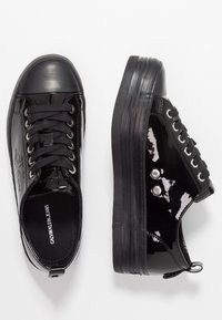 Black patent leather sneakers with flat laces, rounded toe, rubber sole, and silver eyelet details. Smooth texture with glossy finish.