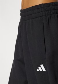 Pantaloni sportivi neri con vita elasticizzata, tasche laterali e un logo bianco a forma di triangolo sulla parte bassa della gamba. Tessuto morbido.