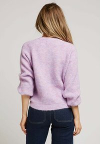 Pull en tricot violet clair avec une texture douce, épaules tombantes et manches trois-quarts, associé à un jeans bleu foncé.