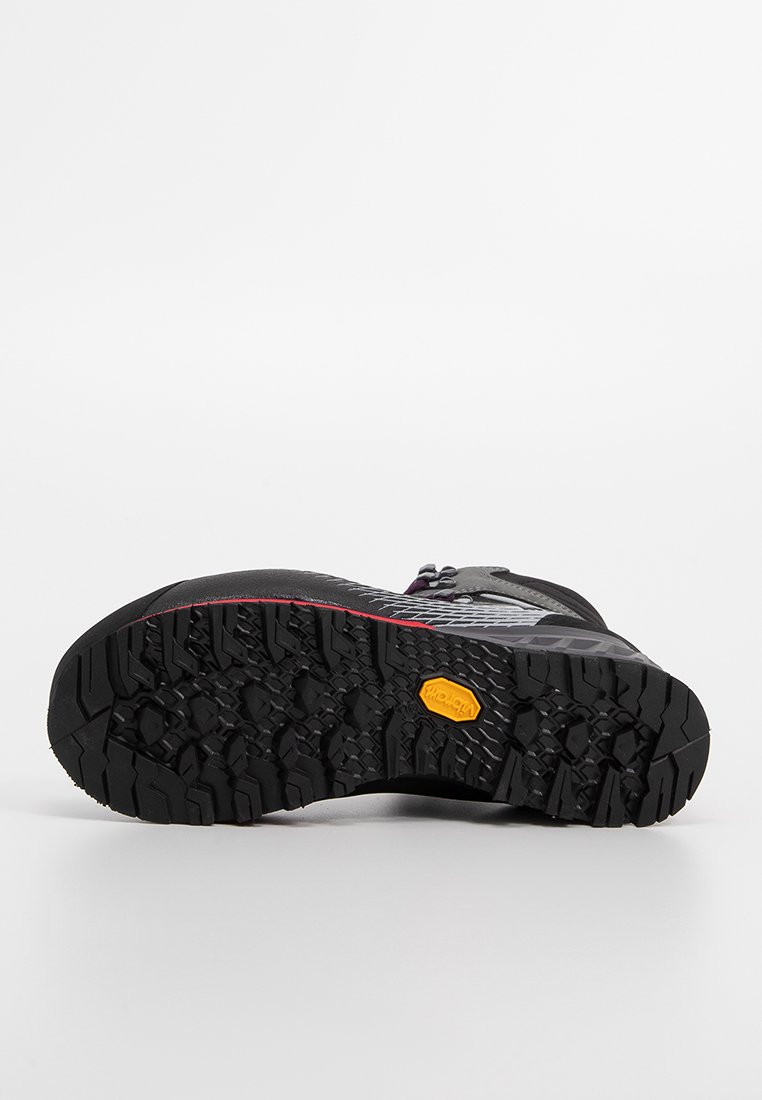 Podeszwa czarnej buty trekkingowej z głębokim bieżnikiem i żółtym logo Vibram, prezentująca się na białym tle.